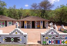 several colorfully painted huts in the middle of a dirt area with trees and bushes behind them