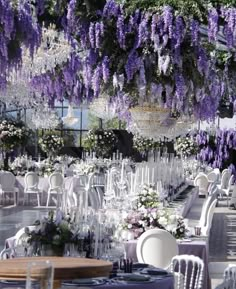 tables and chairs are set up with purple flowers hanging from the ceiling, along with chandeliers