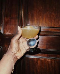 a person holding up a glass filled with liquid on top of a wooden door frame