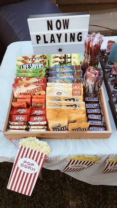 a table topped with popcorn and snacks on top of a white cloth covered field next to a sign that says now playing