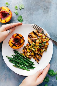 two hands holding a plate with grilled peaches and asparagus