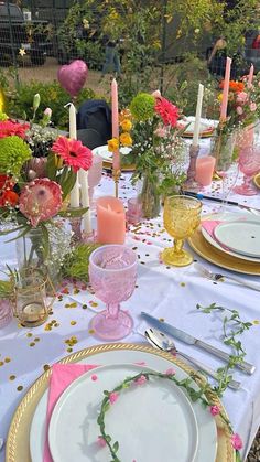 the table is set with pink and yellow flowers in vases, candles, and plates