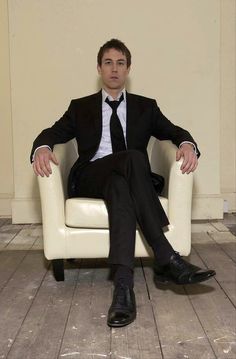 a man in a suit and tie sitting on a white chair with his legs crossed