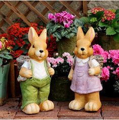 two small statues of rabbits standing next to each other in front of potted flowers