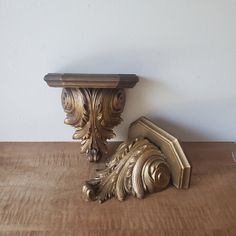 a wooden table topped with a gold vase and two ornately carved wood brackets on top of it