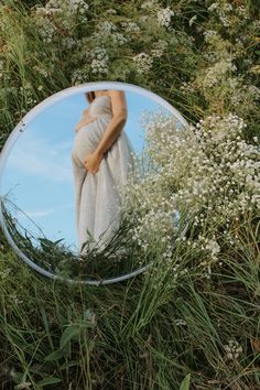 a pregnant woman's reflection in a mirror on the ground surrounded by wildflowers