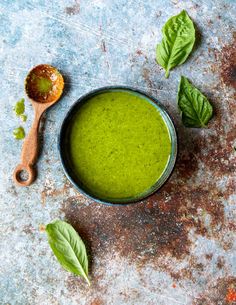 a bowl filled with green liquid next to two spoons on top of a table