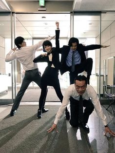 four people in suits and ties are posing for a photo with their hands up while one man is leaning on the ground