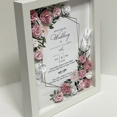 a wedding card with pink and white paper flowers in a square frame on a table