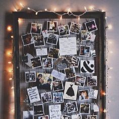 a bulletin board covered in pictures and magnets with lights on the wall behind it