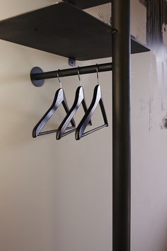 three metal hangers are hanging from a black pole in front of a white wall