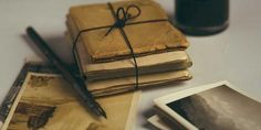 an old book with a pen on top of it next to some photos and a candle