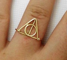 a person's hand with a gold ring on it and a harry potter symbol in the middle