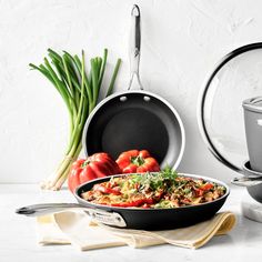 a skillet with tomatoes, onions and other cooking utensils next to it