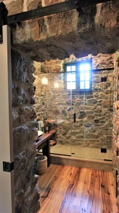 a bathroom with stone walls and wooden flooring next to a glass enclosed shower stall