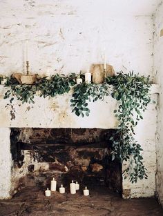 a fireplace with candles and greenery on the mantle