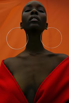 a woman wearing large hoop earrings and a red dress with an orange wall in the background