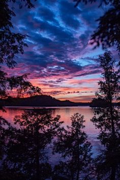 the sky is purple and blue as it sits over water with trees in front of it