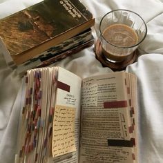 an open book sitting on top of a bed next to a glass filled with liquid