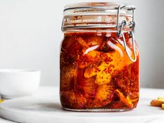 a glass jar filled with pickled vegetables on top of a white counter next to sliced bananas