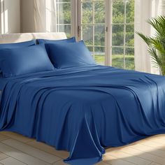 a bed with blue sheets and pillows in front of a large window on the floor