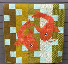 a quilted wall hanging with two red fish on it's side and another one in the background