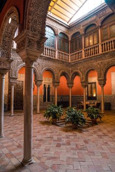 the inside of an old building with columns and arches on it's sides, surrounded by potted plants