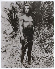 an old black and white photo of a man with no shirt on standing in front of trees