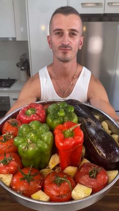 a man sitting in front of a large pan filled with peppers and other food items