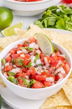 a white bowl filled with salsa surrounded by tortilla chips and lime wedges