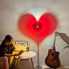 a woman sitting at a table with a guitar next to a red heart shaped lamp