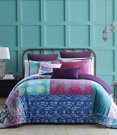 a bed with blue and pink comforters in front of a wall painted aqua green