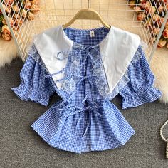 Add a touch of vintage charm to your wardrobe with this delightful blue gingham blouse, featuring intricate lace trims and a classic sailor collar. The blouse showcases a timeless gingham pattern in a fresh blue and white color palette, perfect for a chic and casual look. The oversized sailor collar is adorned with delicate lace detailing, adding a feminine and whimsical touch to the design.The blouse is designed with puff sleeves that have elasticized cuffs, creating a playful and comfortable f Blue Doll Collar Top For Spring, Fitted Blue Tops With Lace Collar, Blue Fitted Top With Lace Collar, Blue Peter Pan Collar Blouse For Spring, Cottagecore Short Sleeve Top With Lace Collar, Spring Blouse With Lace Trim And Cute Collar, Blue Short Sleeve Blouse With Lace Trim, Spring Tops With Lace Trim And Cute Collar, Cottagecore Tops With Peter Pan Collar For Summer