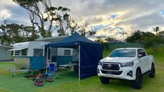 a white truck parked next to a blue tent on top of a grass covered field