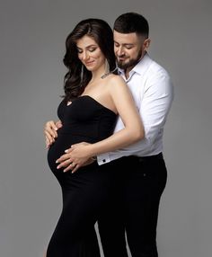 a pregnant couple posing for a photo in their black gowns and white shirt, with one holding the other's belly