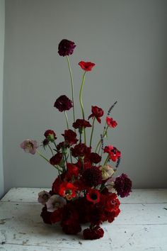 a vase filled with red and purple flowers on top of a wooden table next to a white wall