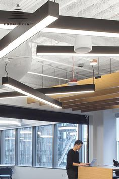 a man is standing at a desk in an office with large windows and lots of light