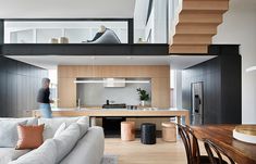 a living room filled with furniture next to a wooden table and stair case in front of a kitchen