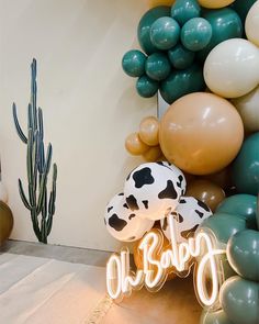 a neon sign that says oh baby next to some balloons and a cactus in the background