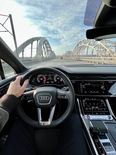 a person driving an audi car on a bridge in the background with a hand on the steering wheel