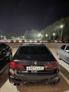 two cars are parked in a parking lot at night, one is black and the other is silver