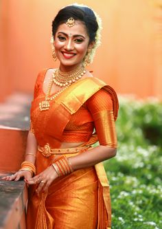 a woman in an orange and gold sari with her hand on her hip, smiling