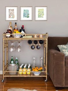 a gold bar cart with bottles and glasses on it in front of a brown couch