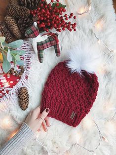 a woman's hand on top of a red knitted hat next to christmas decorations