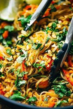 a bowl filled with noodles and vegetables on top of a wooden table next to two tongs