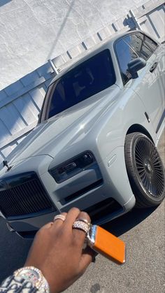 a person is holding an orange object in front of a gray car with its hood up