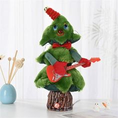 a green stuffed animal with a red guitar in it's lap, sitting on a tree stump