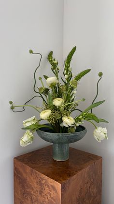 a vase filled with white flowers sitting on top of a wooden table next to a wall