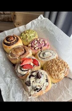 a bunch of doughnuts that are on some wax paper with strawberries and other pastries