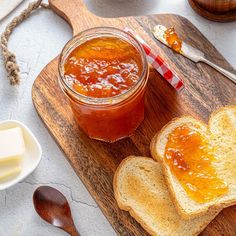 two pieces of bread sit on a cutting board next to a jar of jelly and butter